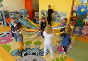 Dzieci poruszają się po obwodzie koła, trzymają w ręku wstążki od wiatraka matematycznego, w środku stoi chłopiec.
